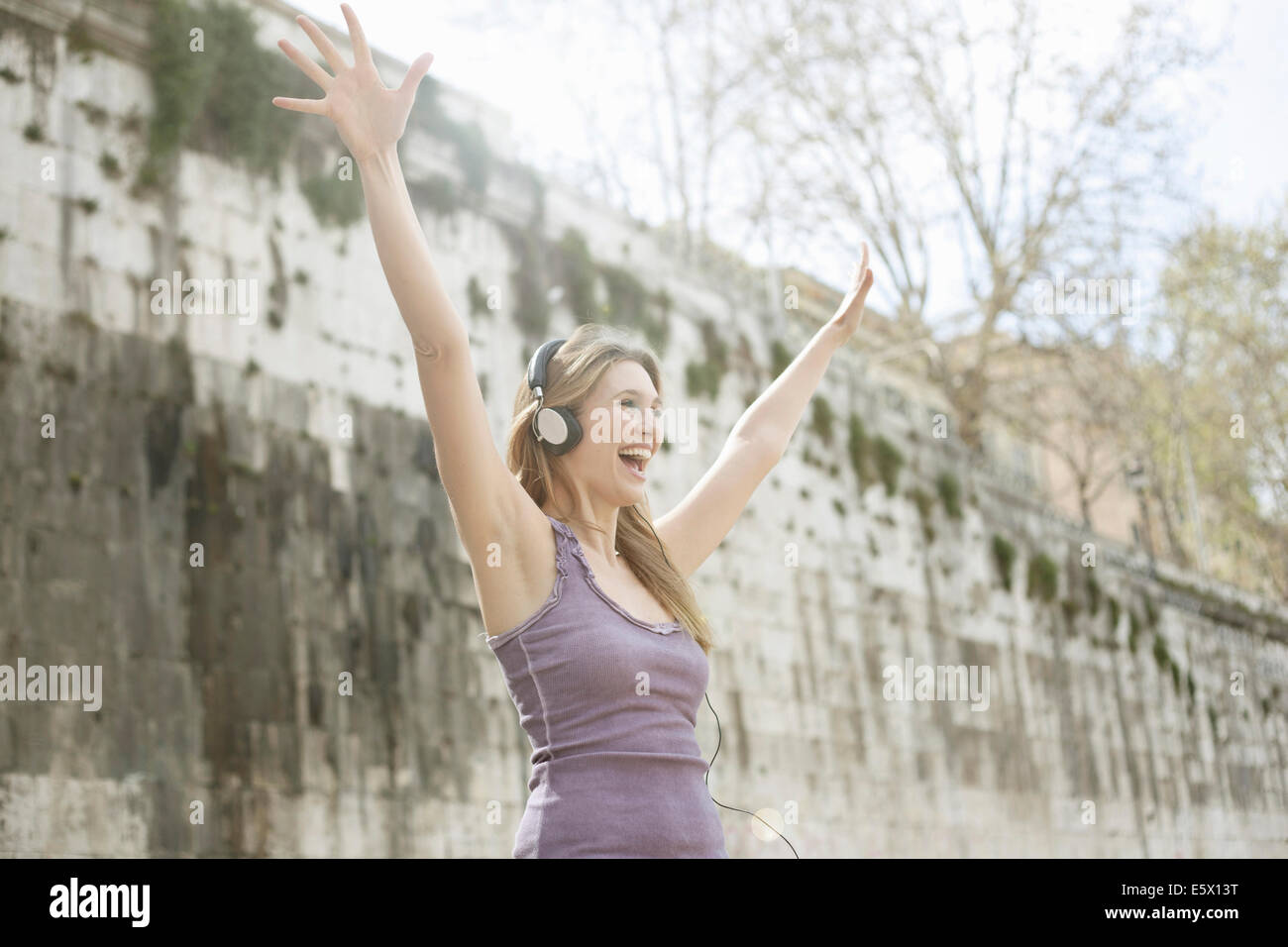 Happy young woman, wearing headphones and raising arms Stock Photo