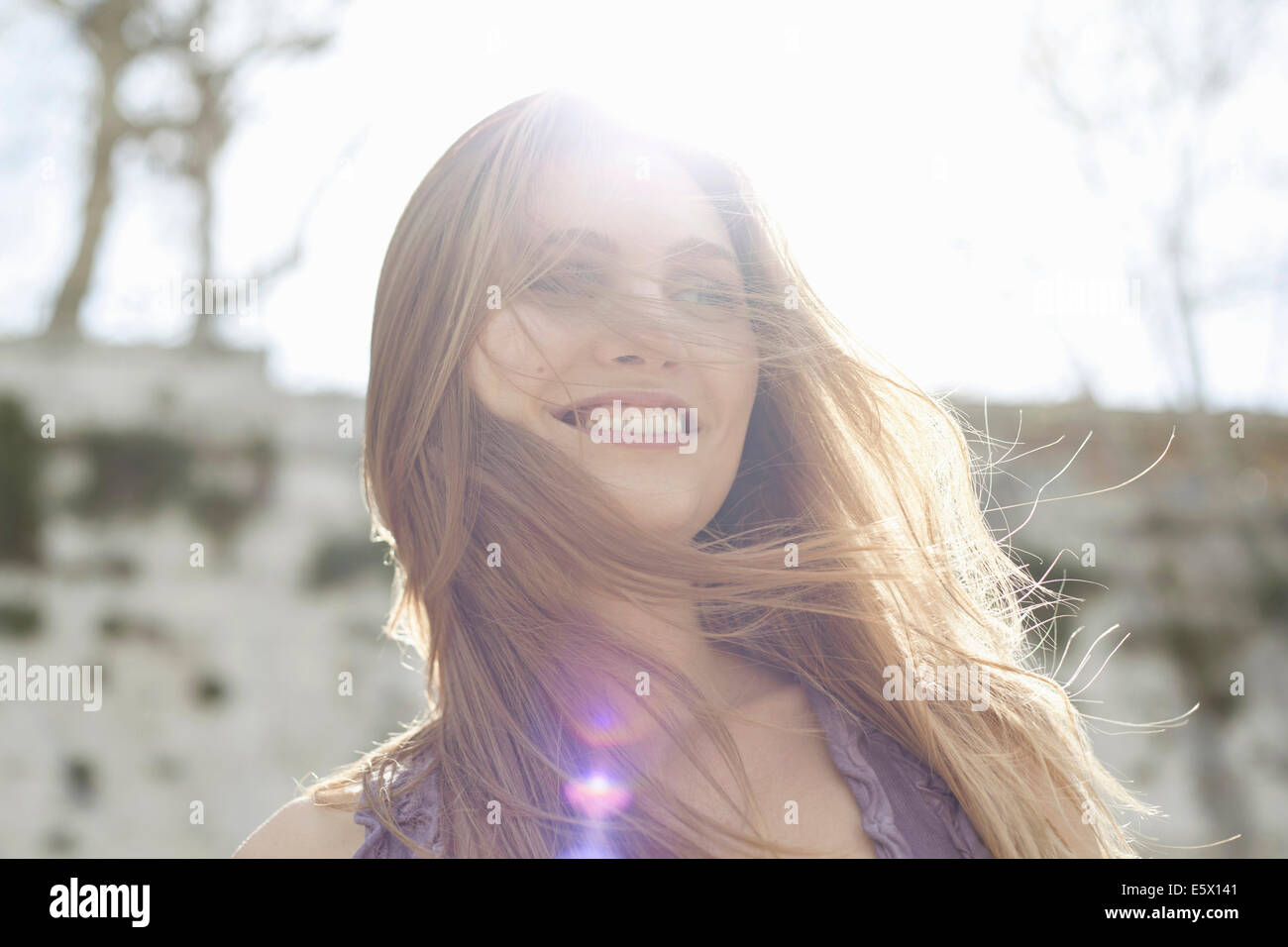 Happy young woman in sunlight, hair blowing over face Stock Photo