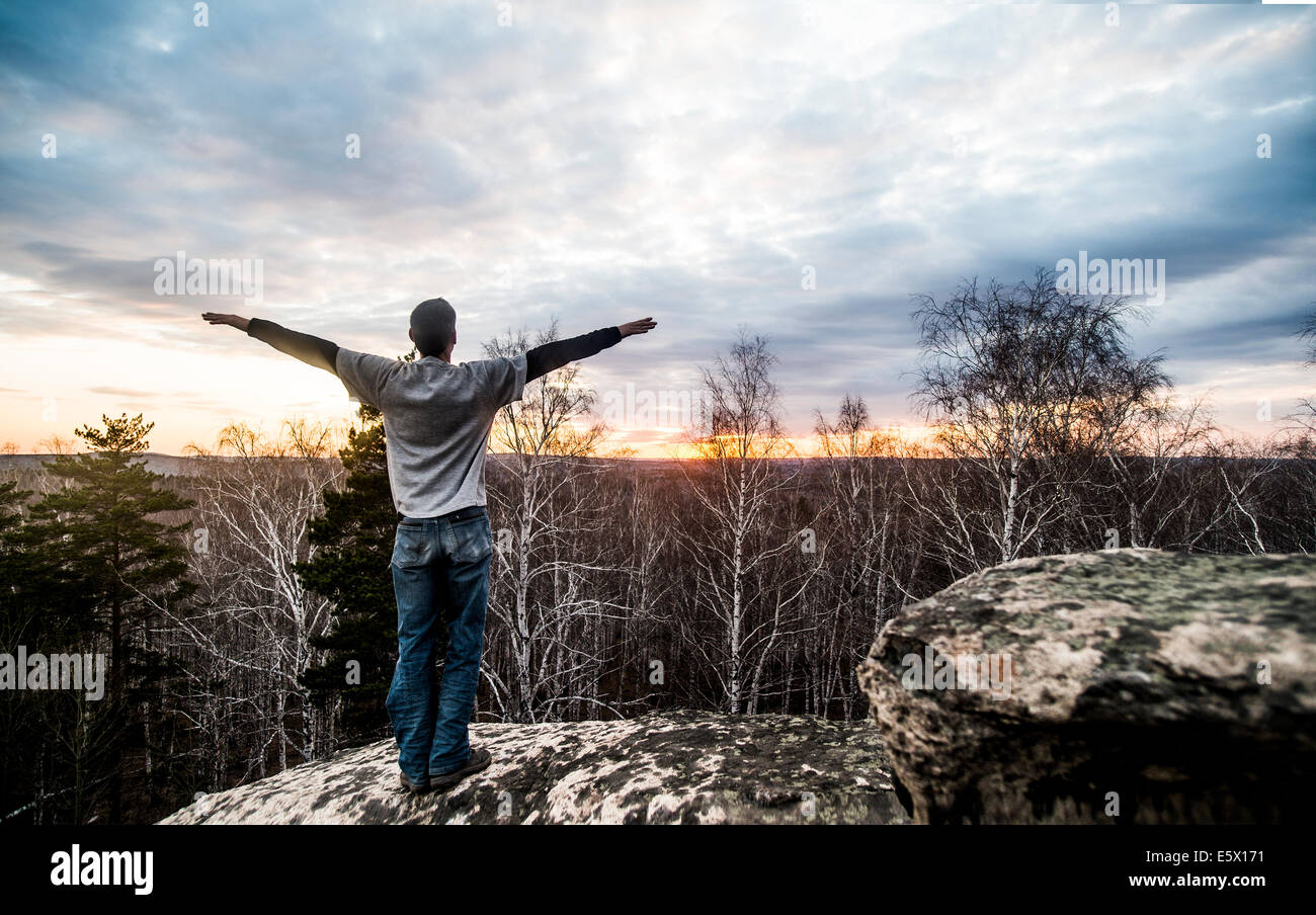 Young man with arms outstretched on top of rock formation at sunset Stock Photo