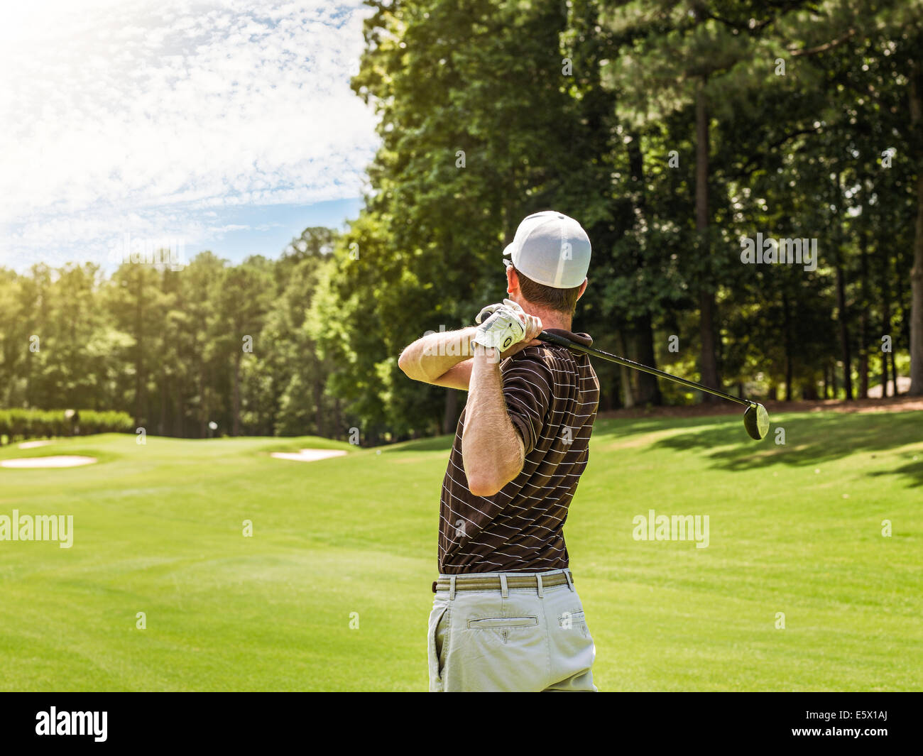 Rear waist up view of young male golfer teeing off on golf course, Apex