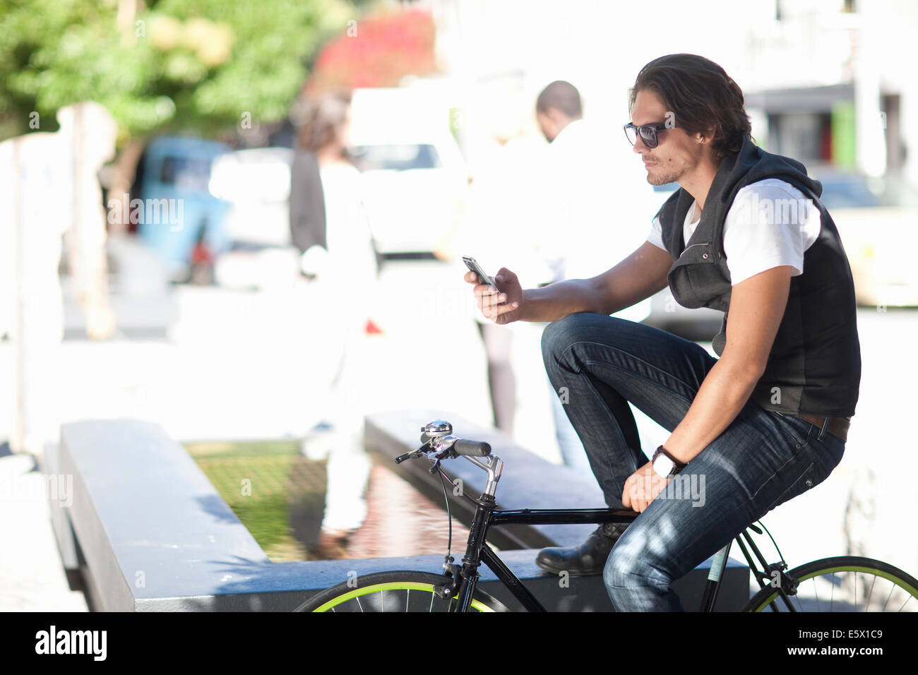 Mid adult male cyclist texting on smartphone on street Stock Photo
