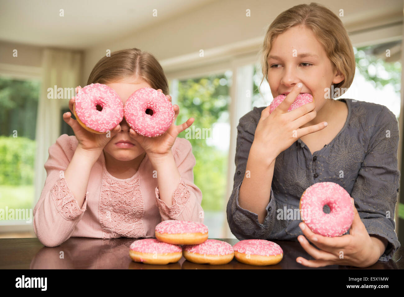 Two sisters one with doughnut holes over her eyes, the other eating Stock Photo