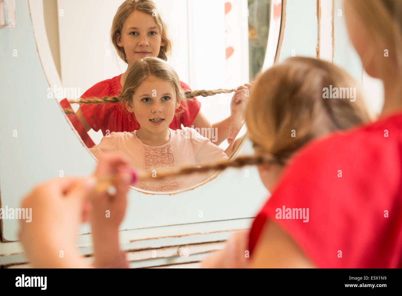 Sisters holding up plaits in bedroom mirror Stock Photo