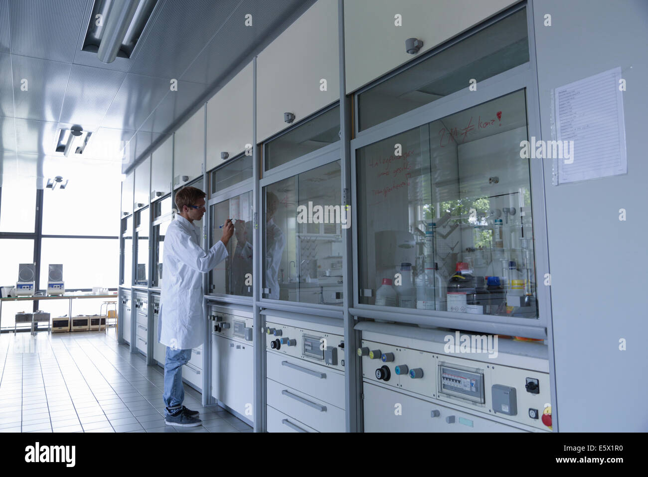 Young male scientist writing on fume cupboard window Stock Photo