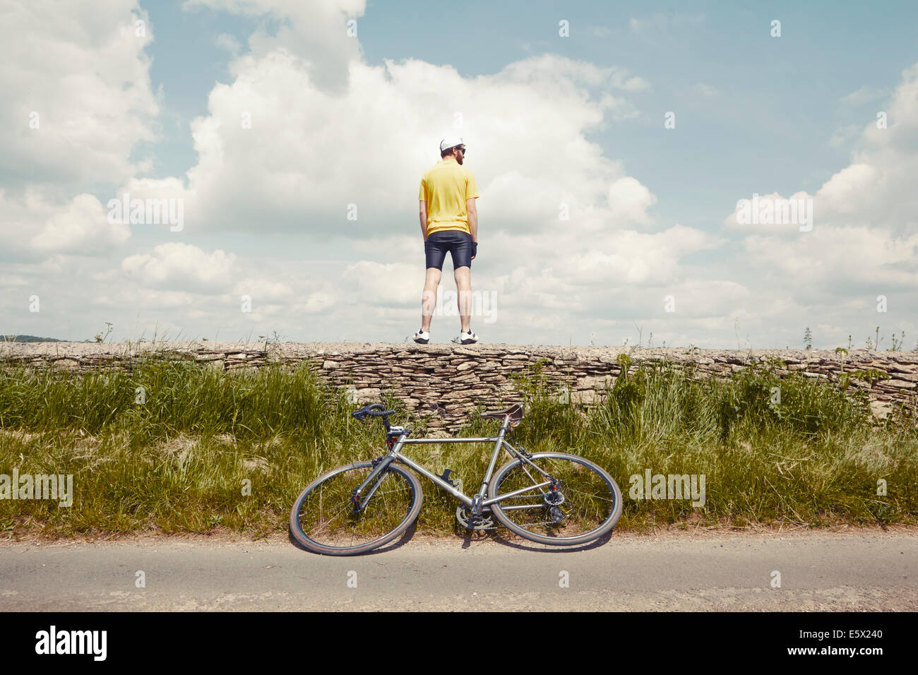 Cyclist standing on stone wall, Cotswolds, UK Stock Photo