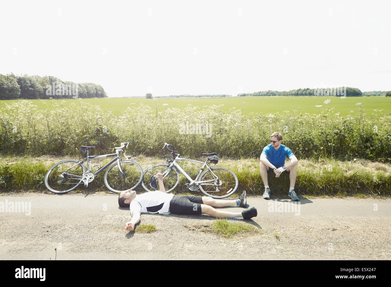 Cyclists lying on ground by fields, Cotswolds, UK Stock Photo