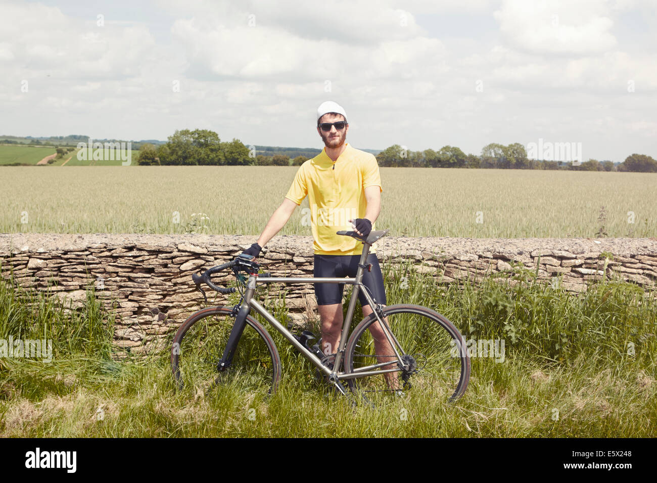 Cyclist standing by stone wall, Cotswolds, UK Stock Photo