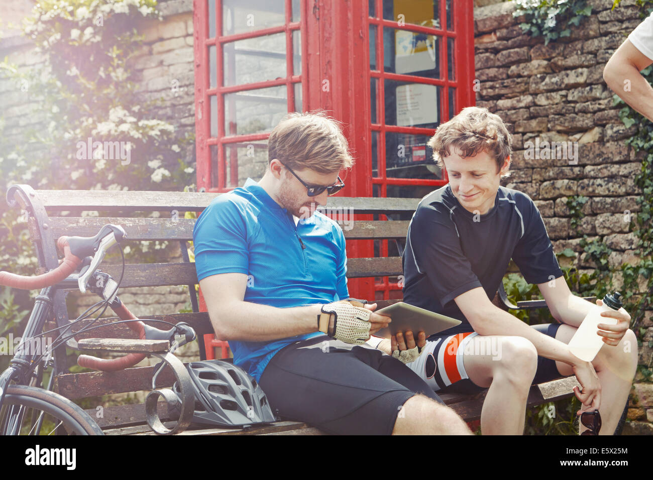 Cyclists using digital tablet by red telephone box, Cotswolds, UK Stock Photo
