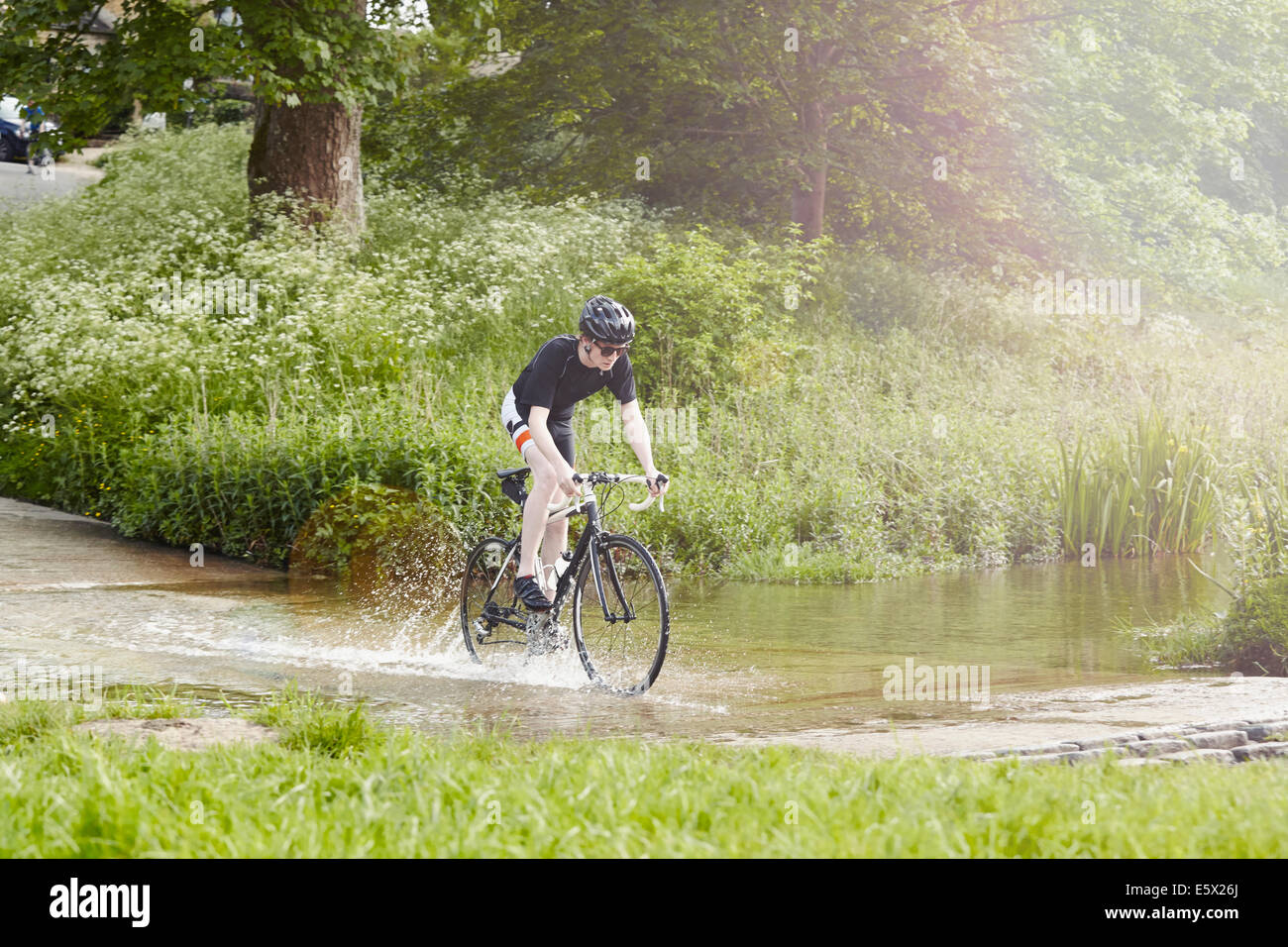 Cyclist riding over flooded road, Cotswolds, UK Stock Photo