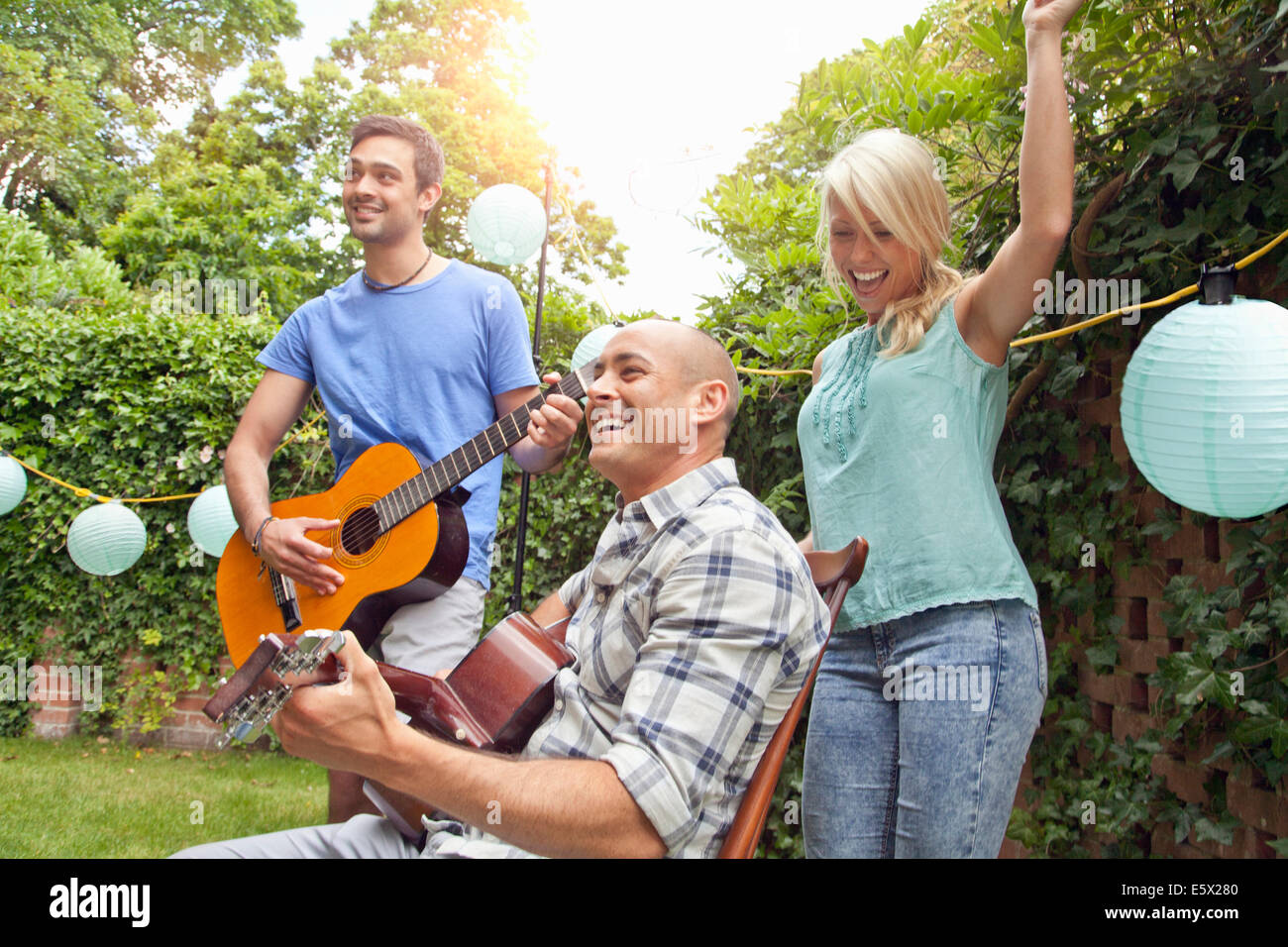 Male friends playing acoustic guitar in garden and young woman dancing Stock Photo