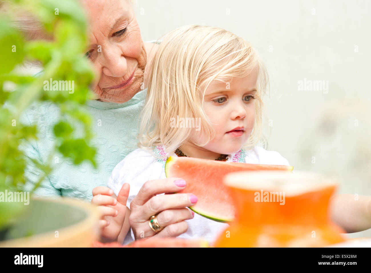 Senior woman and toddler great granddaughter eating melon slice at garden table Stock Photo