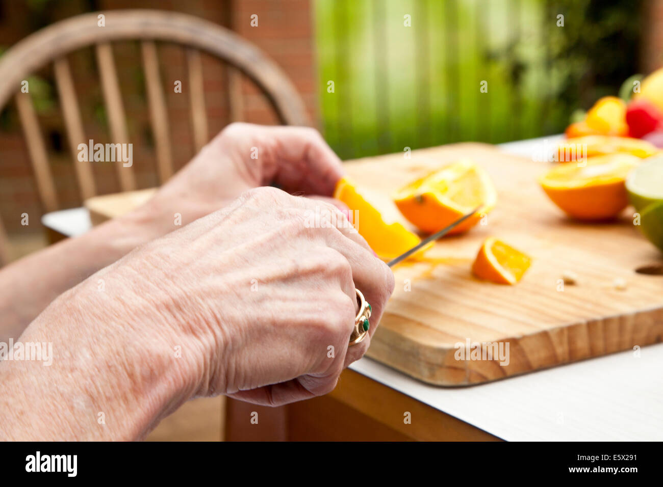 Hands of senior woman slicing oranges at garden table Stock Photo