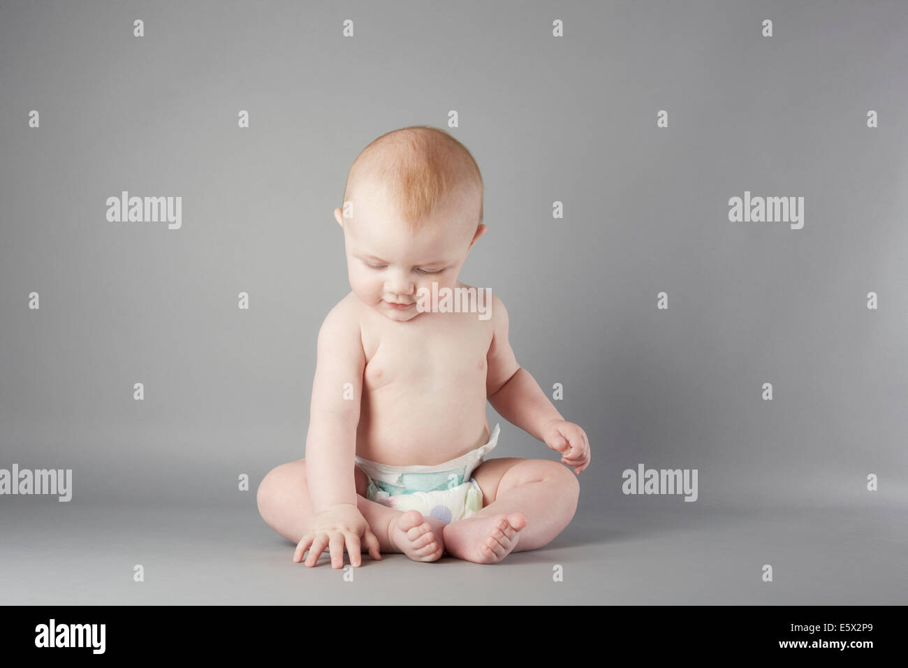 Studio portrait of baby boy sitting up and touching floor Stock Photo