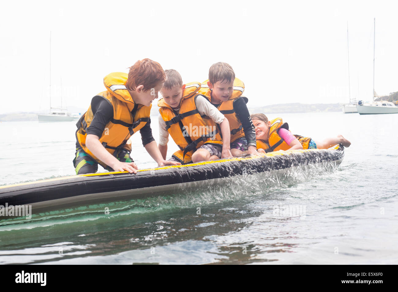 Brothers and sister about to fall from paddleboard into sea Stock Photo