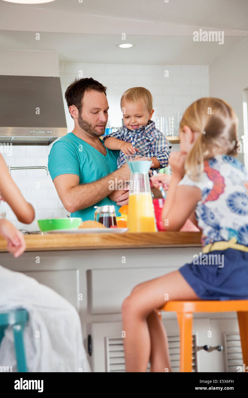 Father multi tasking breakfast with son and daughters Stock Photo