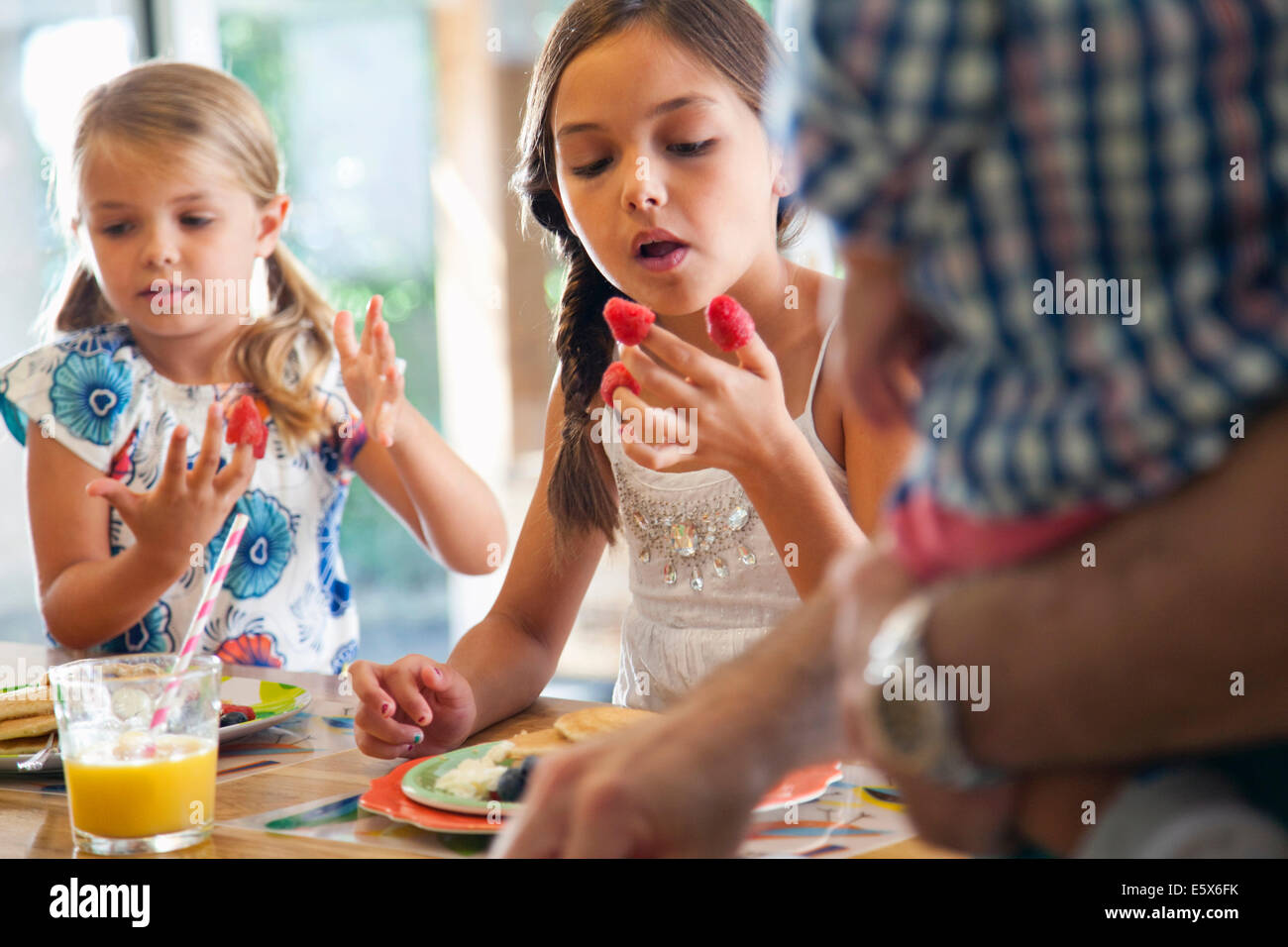 Two sisters with raspberries on their fingers at kitchen breakfast bar Stock Photo