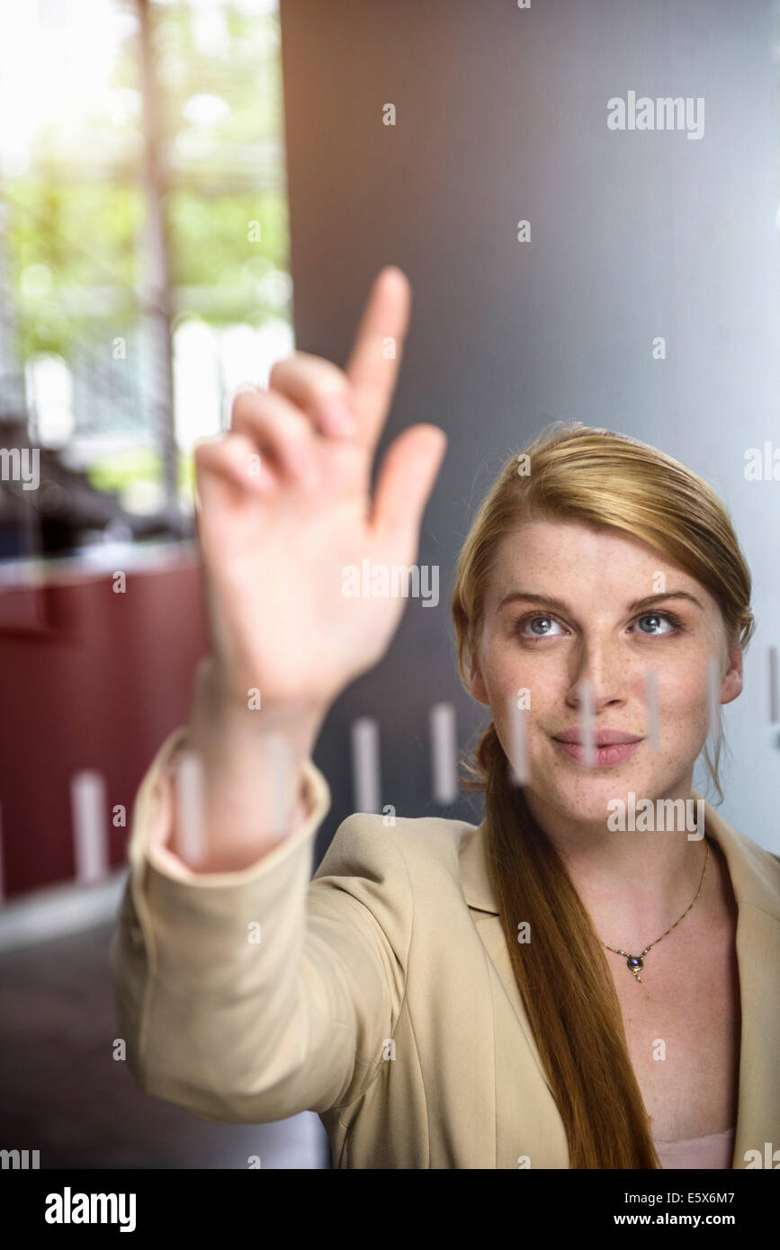 Young businesswoman writing message on glass wall with finger Stock