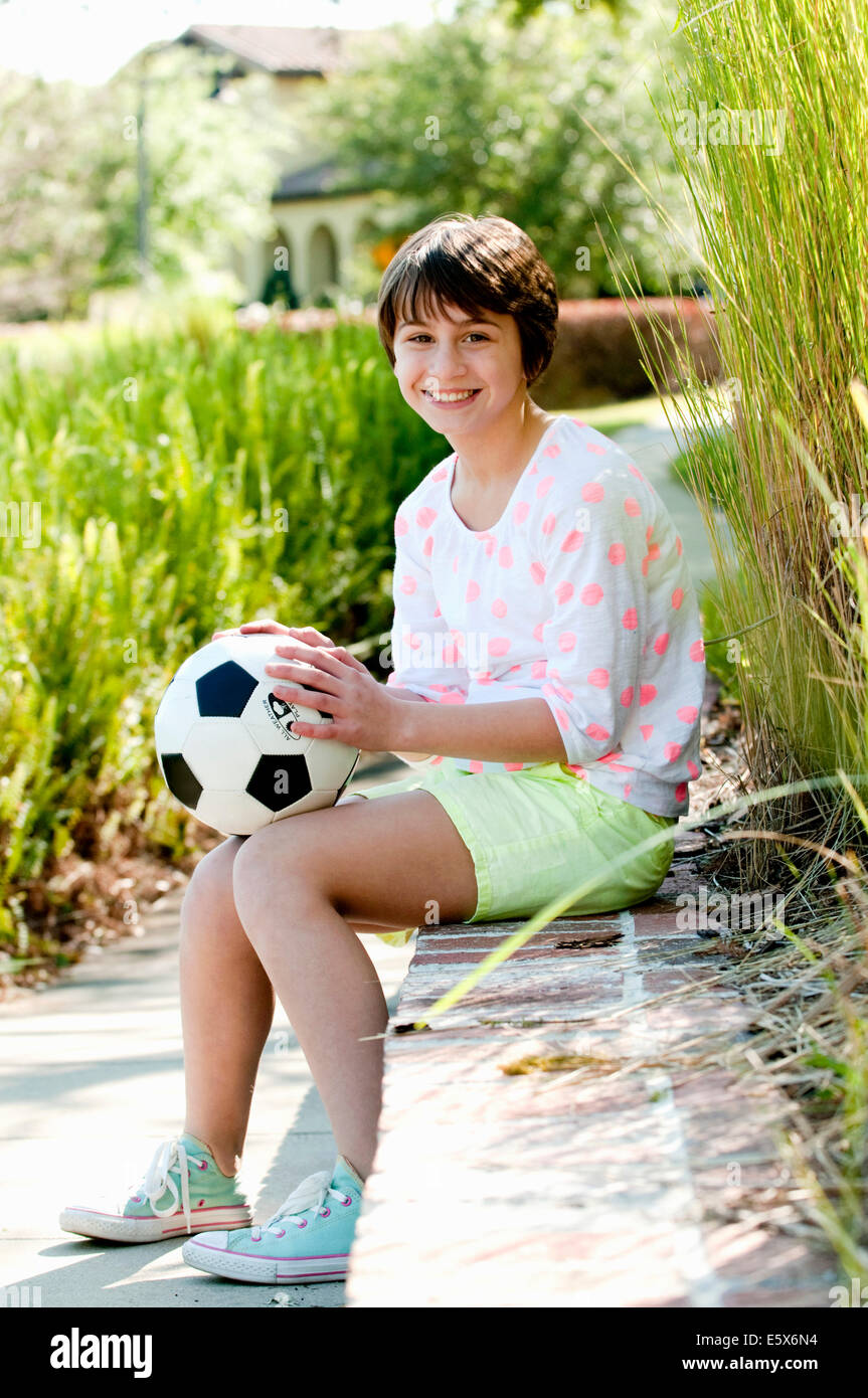 Portrait of ten year old girl sitting on park wall with soccer ball