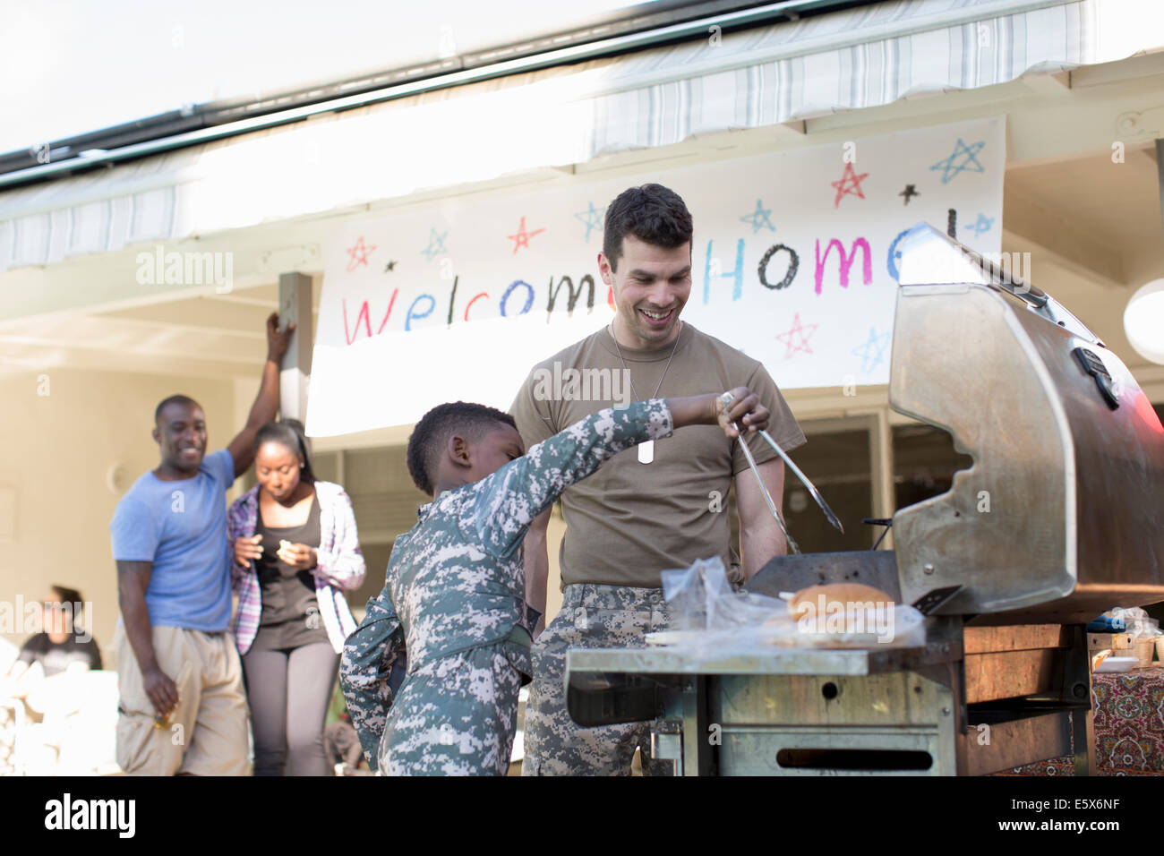 Boy barbecuing burgers with male soldier at homecoming party Stock Photo
