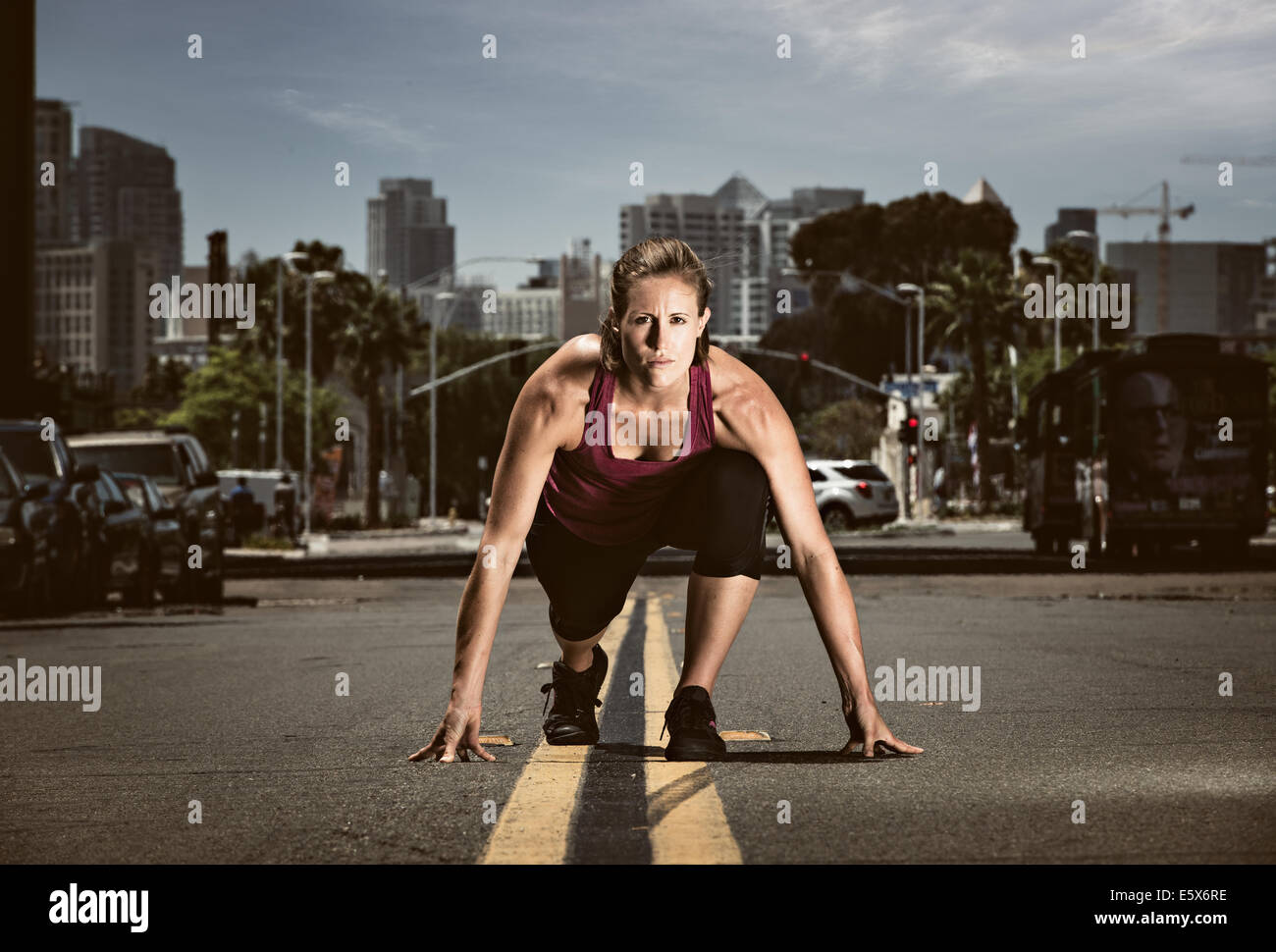 Young adult woman in start position in road, getting ready to run Stock Photo
