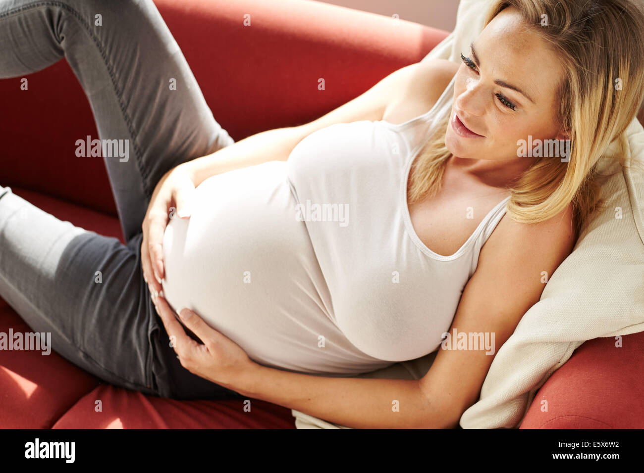 Pregnant woman sat relaxing on sofa Stock Photo