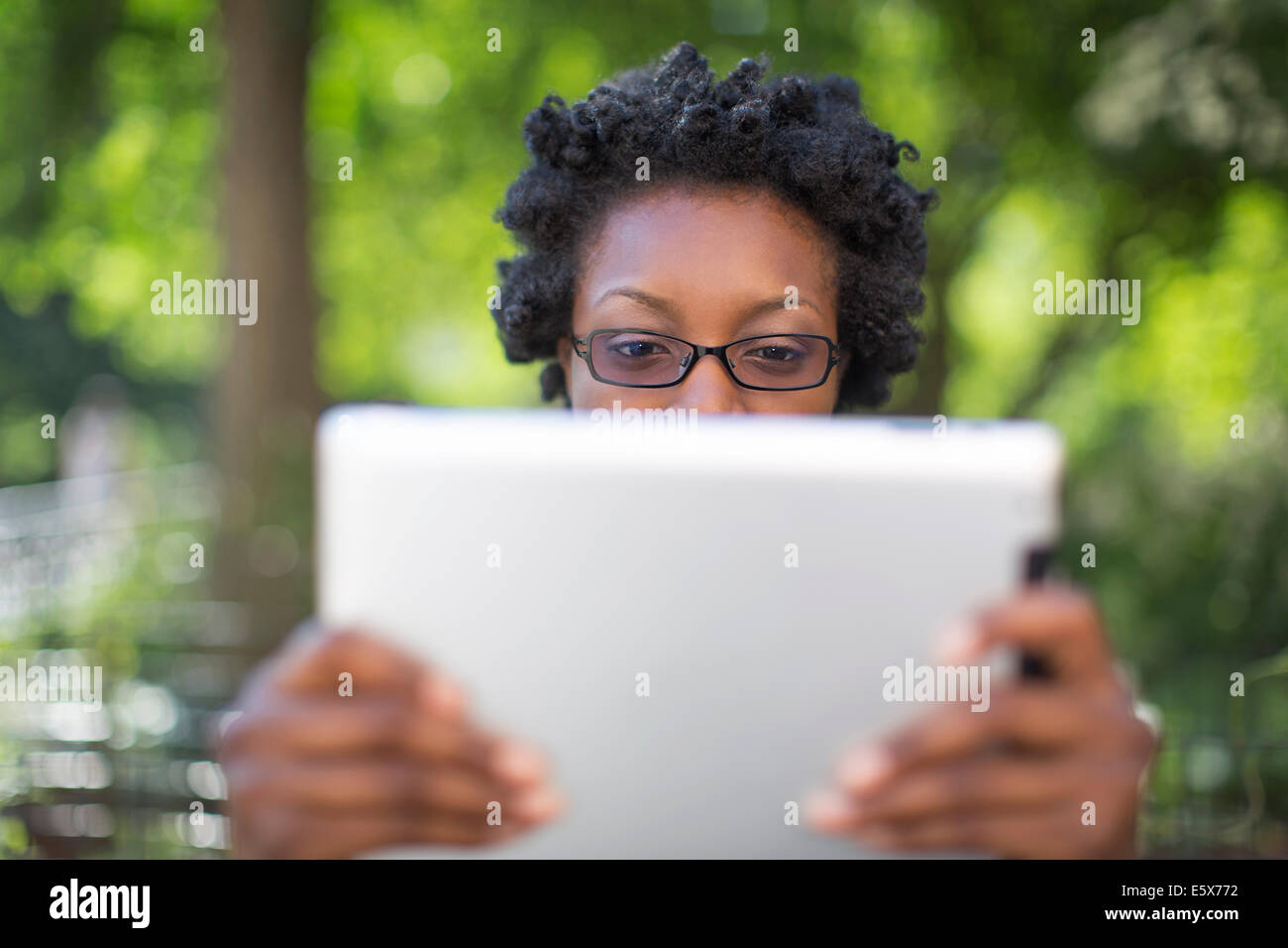 Young woman in park holding up and reading digital tablet Stock Photo