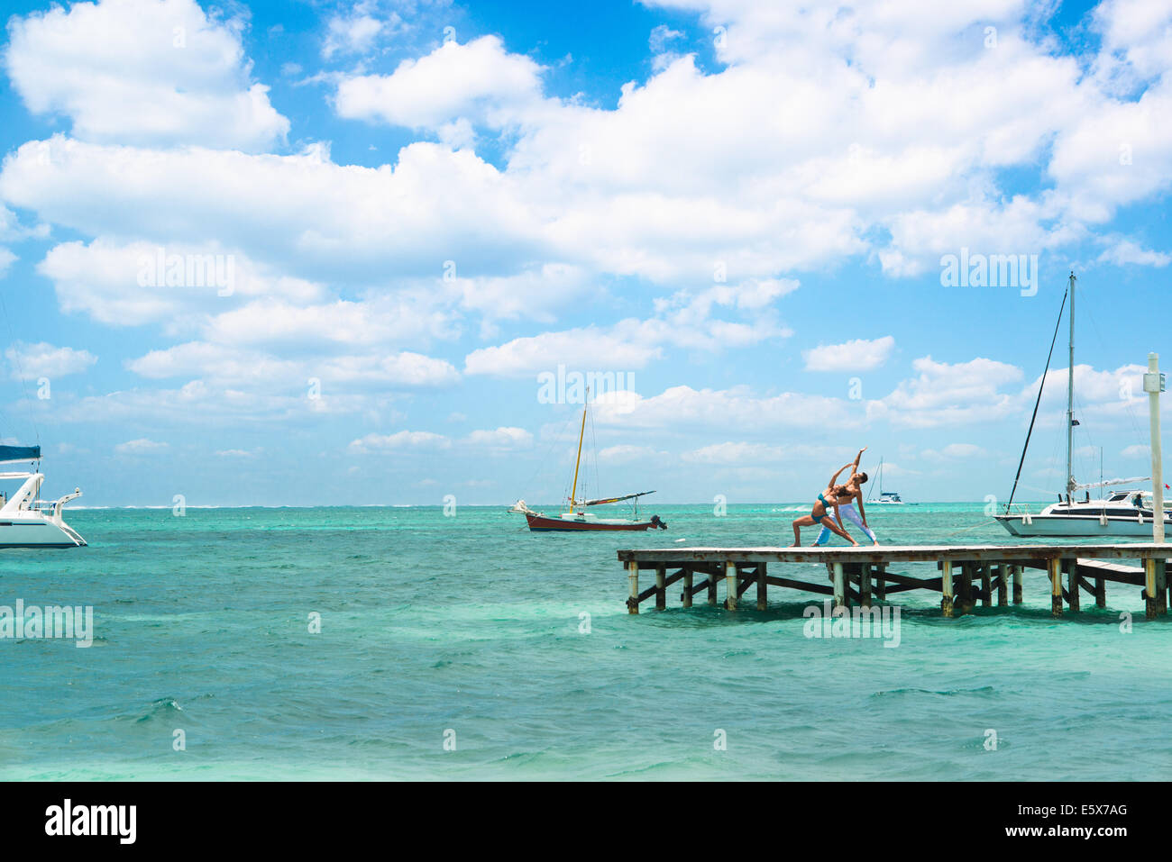 Young couple practising yoga on pier, San Pedro, Belize Stock Photo