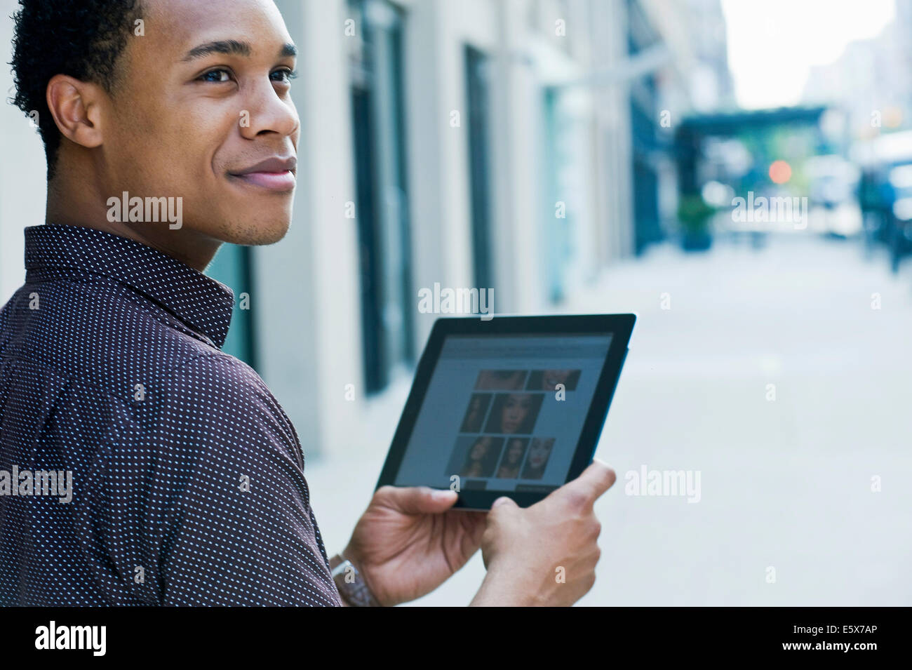 Young man on city street using digital tablet and looking over shoulder Stock Photo