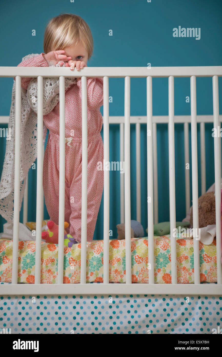 Portrait of female toddler hiding behind comfort blanket in crib Stock
