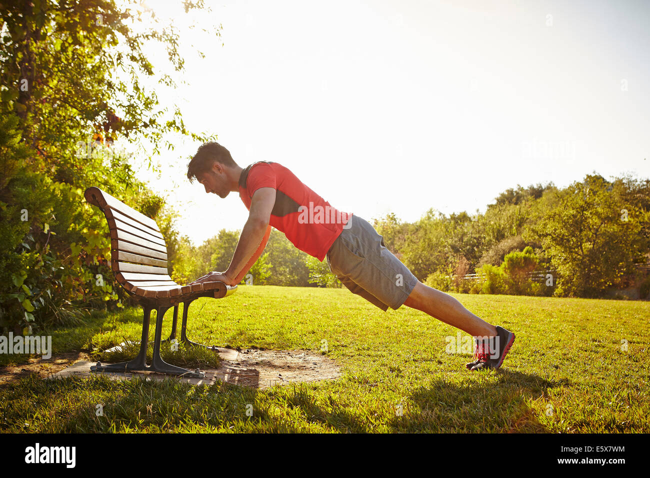 Young male runner doing push ups on park bench Stock Photo