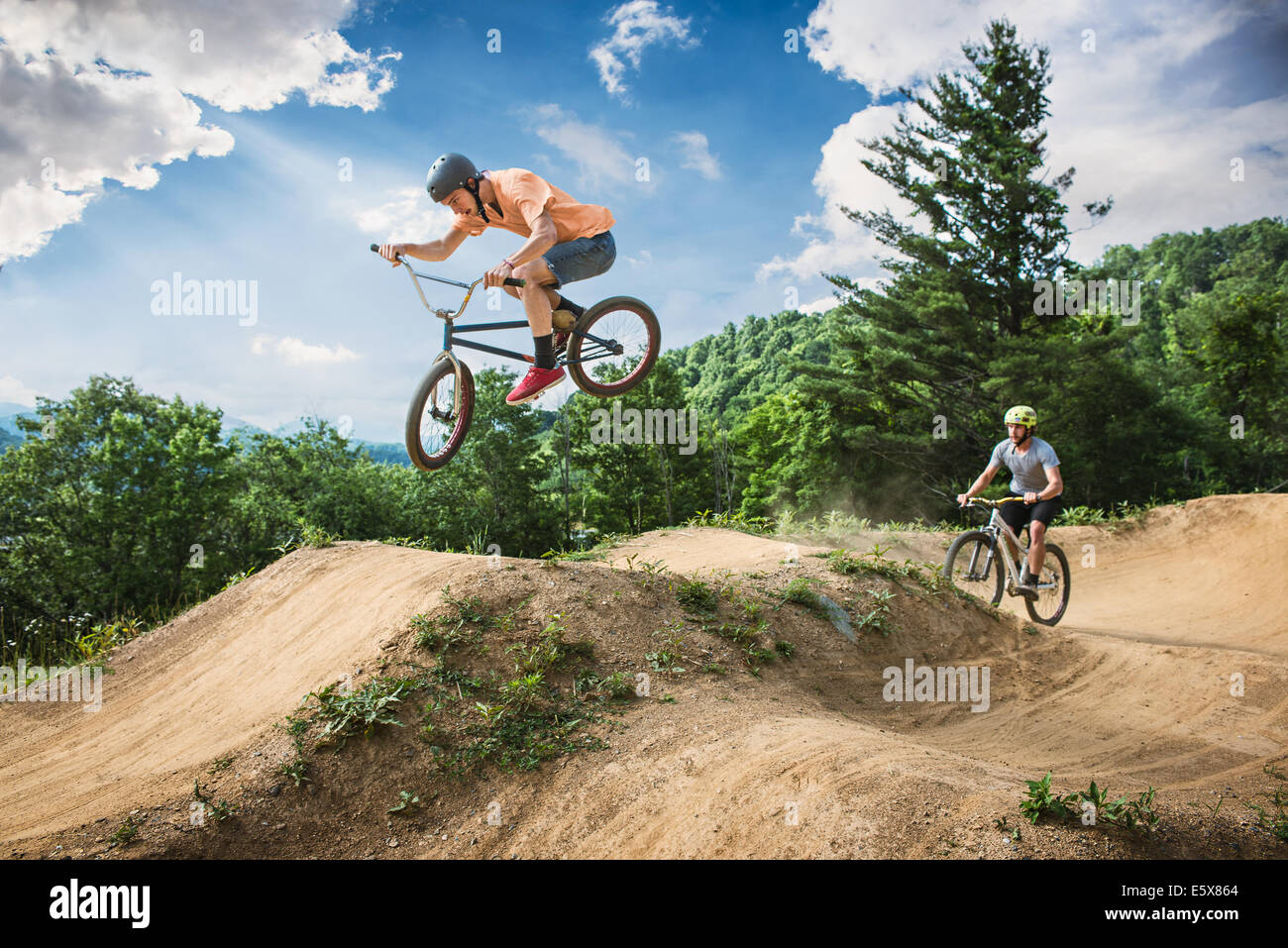 Two male friends riding BMX and mountain bikes on rural pump track Stock Photo