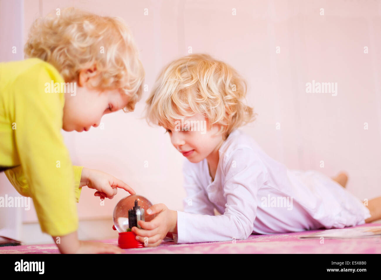 Two young brothers lying on rug gazing at snow globe Stock Photo