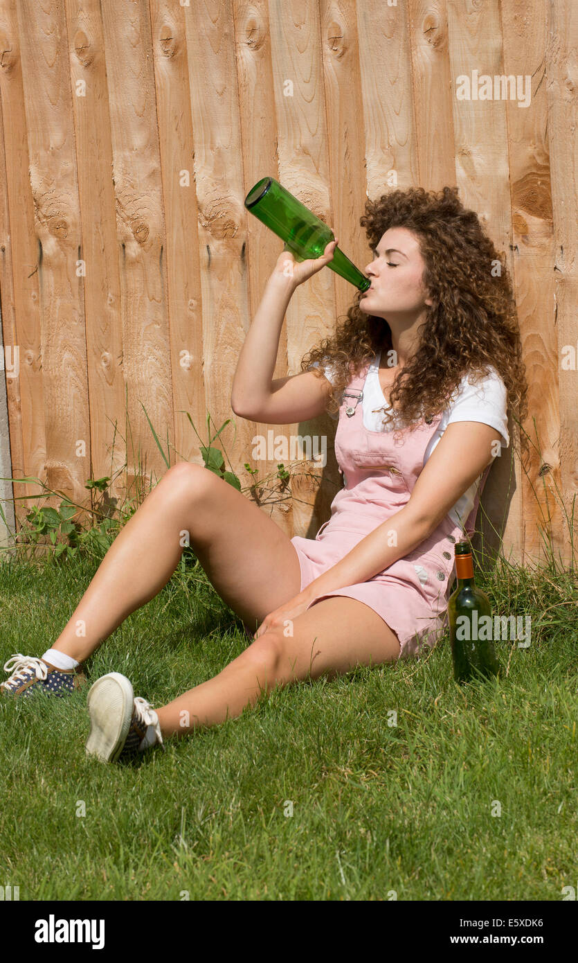 Teenage girl leaning on garden fence drinking alcohol from a glass bottle Stock Photo