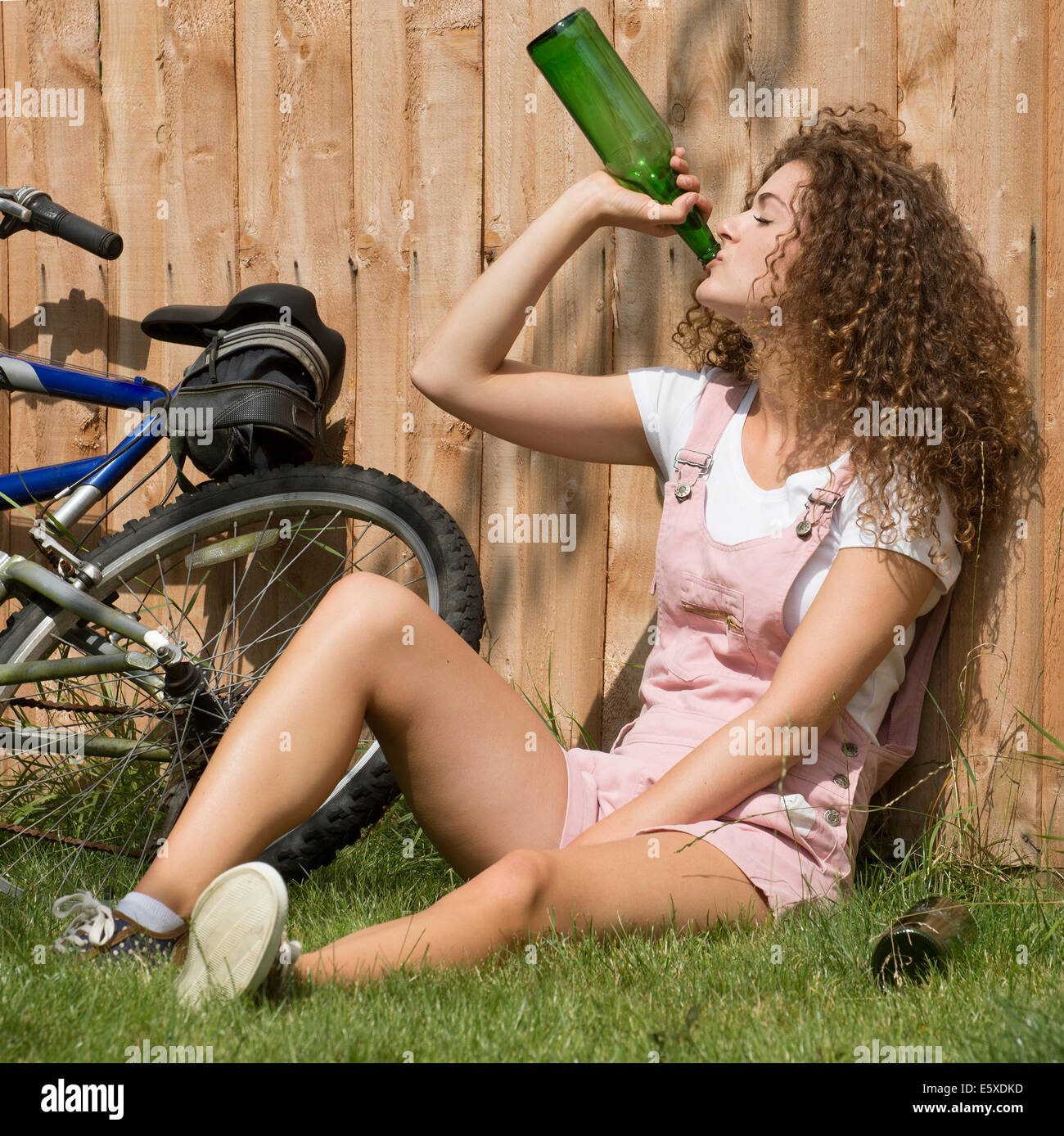 Teenage girl leaning on garden fence drinking alcohol from a glass bottle Stock Photo
