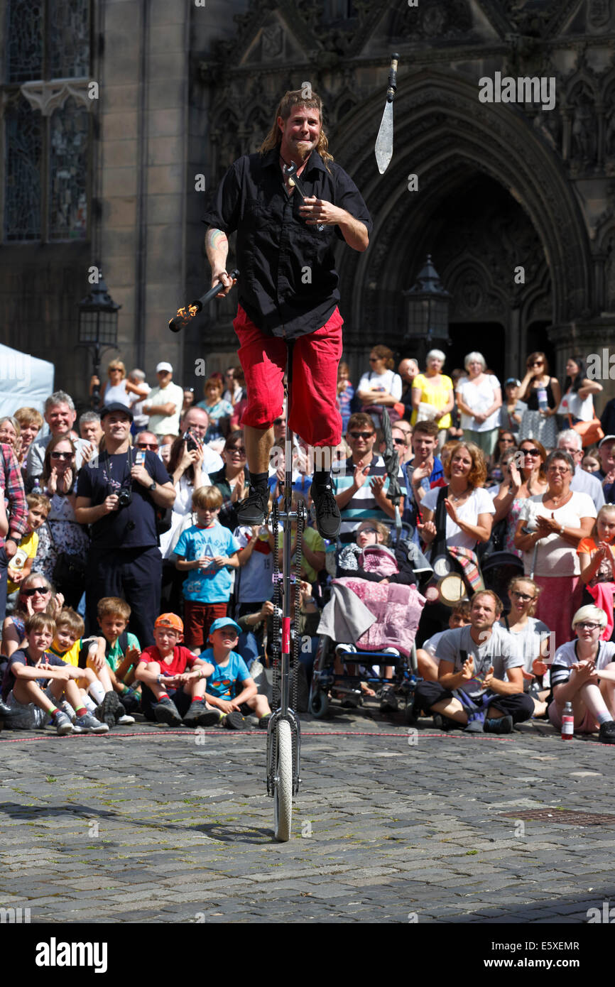 West Parliament Square, Edinburgh, Scotland, UK, Thursday, 7th August, 2014. Street Performer Mullet Man from New Zealand entertaining a crowd with juggling on a uni cycle during the Edinburgh Festival Fringe beside St Giles Cathedral Stock Photo