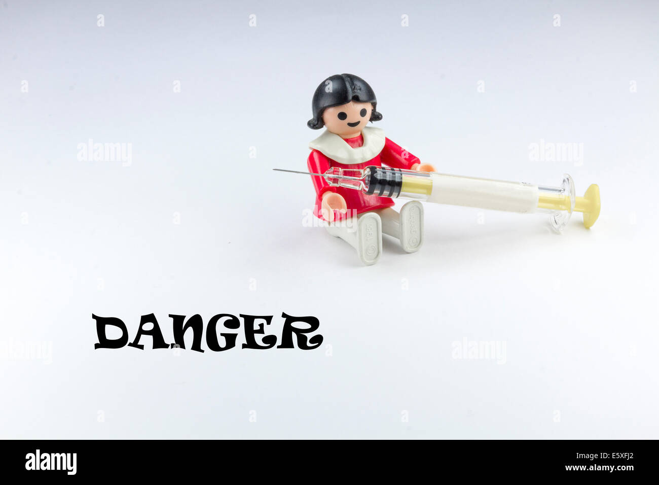 Doll playing with a syringe and warning sign Stock Photo
