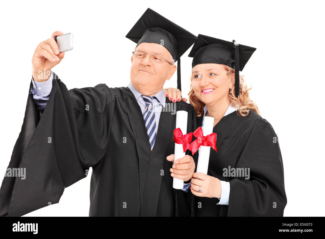 Mature male and female in graduation gowns taking a selfie Stock Photo