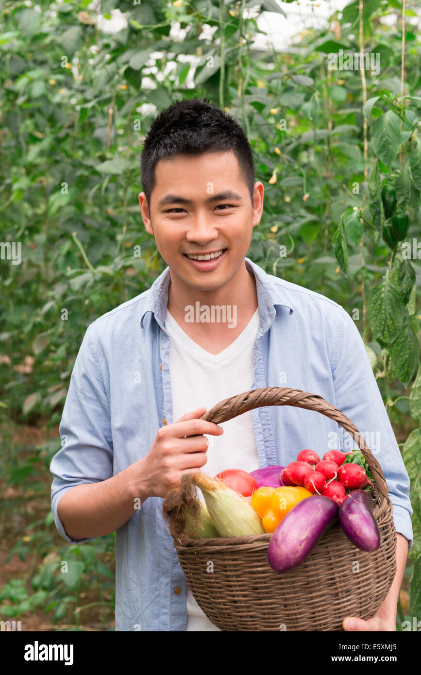 Young farmer holding a basket of fresh vegetables, enjoying harvest ...