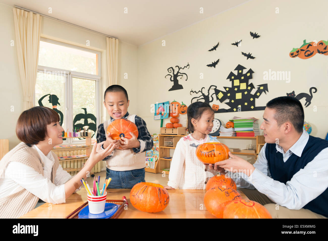 Teachers and students carving pumpkins in classroom, smiling. Stock Photo