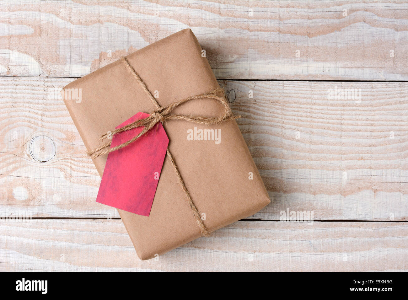 High angle shot of a plain brown paper wrapped Christmas present on a whitewashed wood table. The gift is tied with twine with a Stock Photo