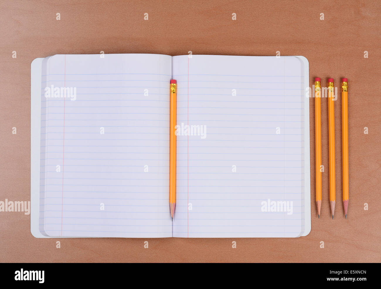 An open theme book with a pencil in the fold and three more sharpened pencils to the side. Horizontal format on a wood classroom Stock Photo