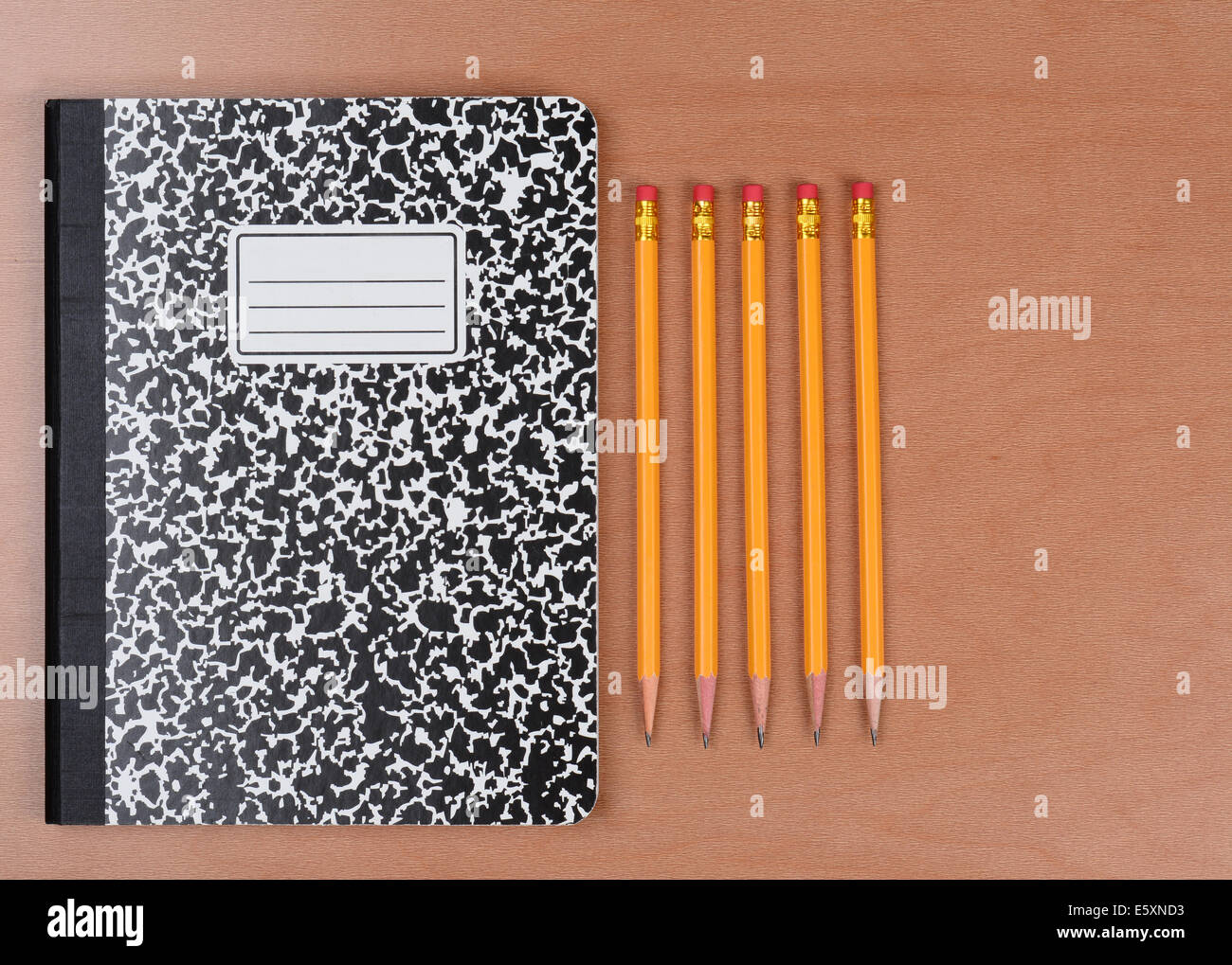 Five sharpened pencils next to a closed theme book on a wood classroom desk. Horizontal format shot form a high angle. Stock Photo