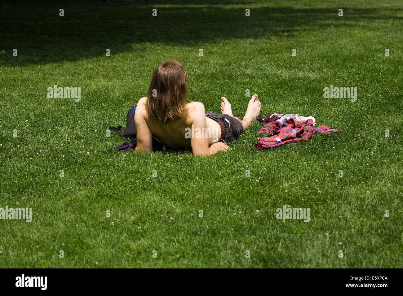 A man with long hair lies in green grass without a shirt on a sunny day