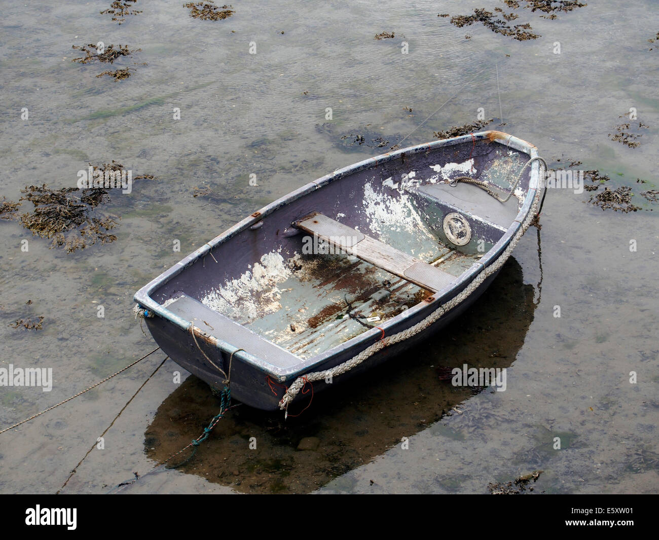 Scruffy praam (or pram) dinghy resting on the muddy bed of a harbour at low tide. Stock Photo