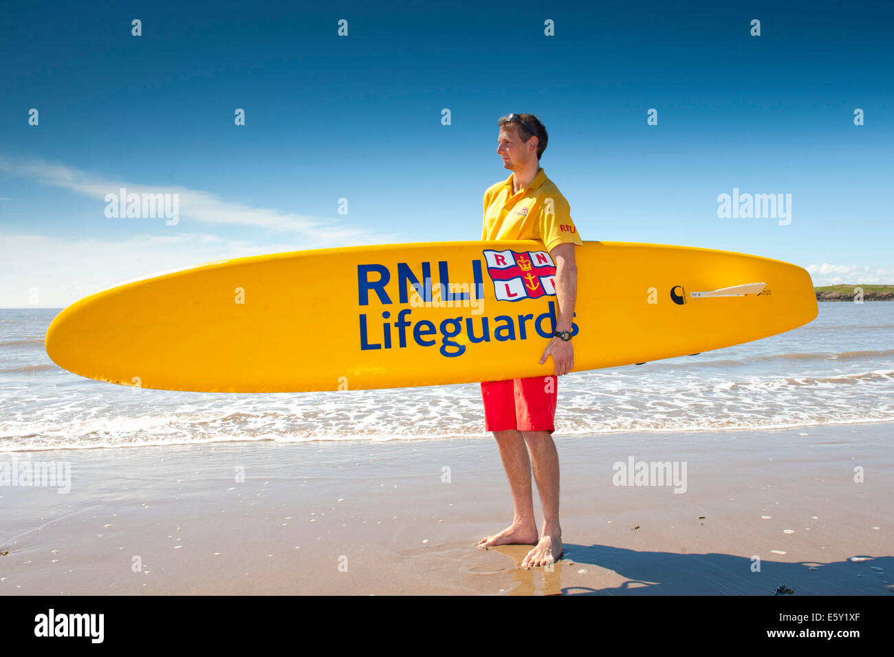 A RNLI (Royal National Lifeboat Institution) lifeguard holds a surf boa during training on Barry Island beach in South Wales. Stock Photo