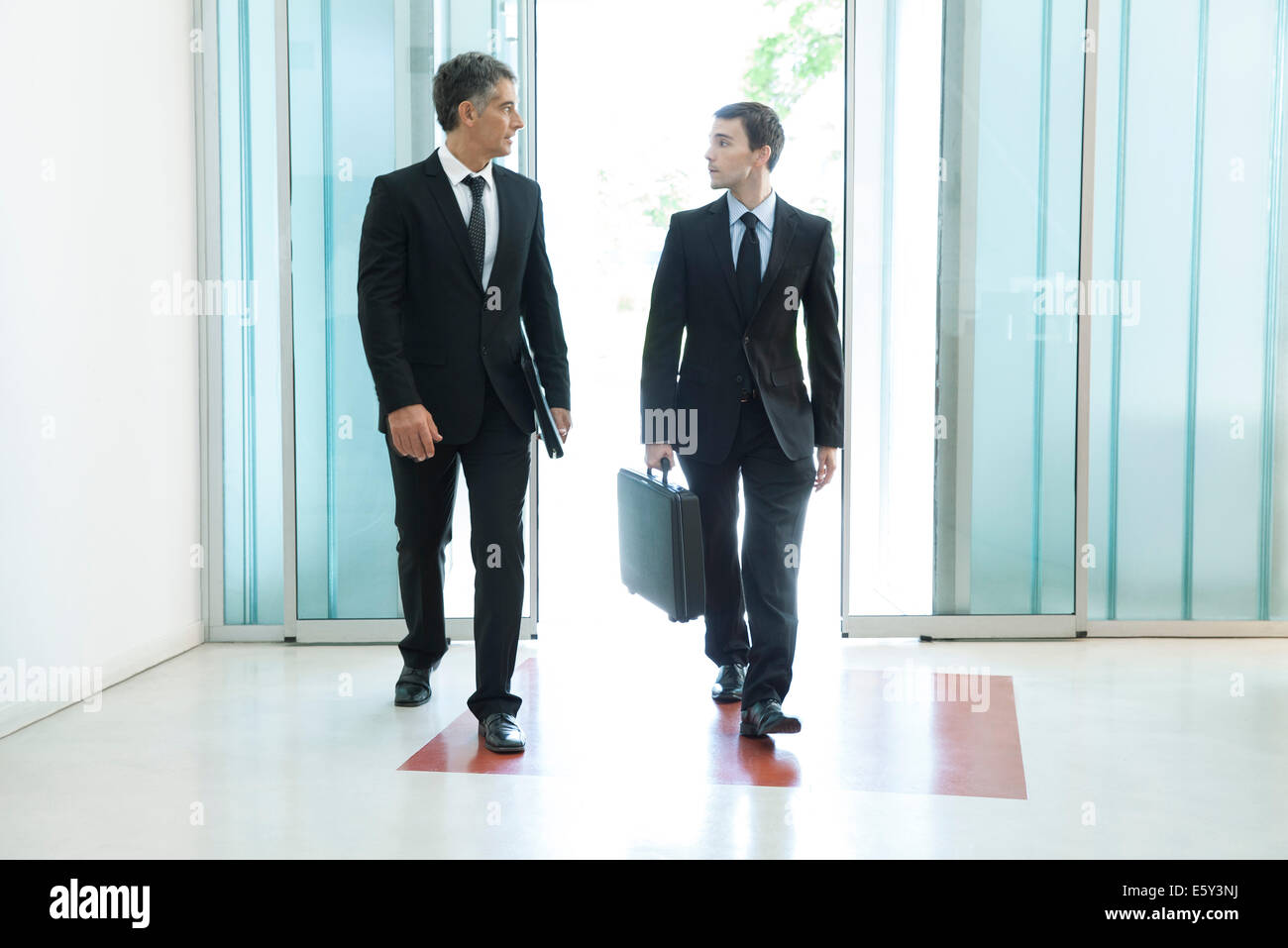 Senior business executive chatting with new associate as they enter building together Stock Photo