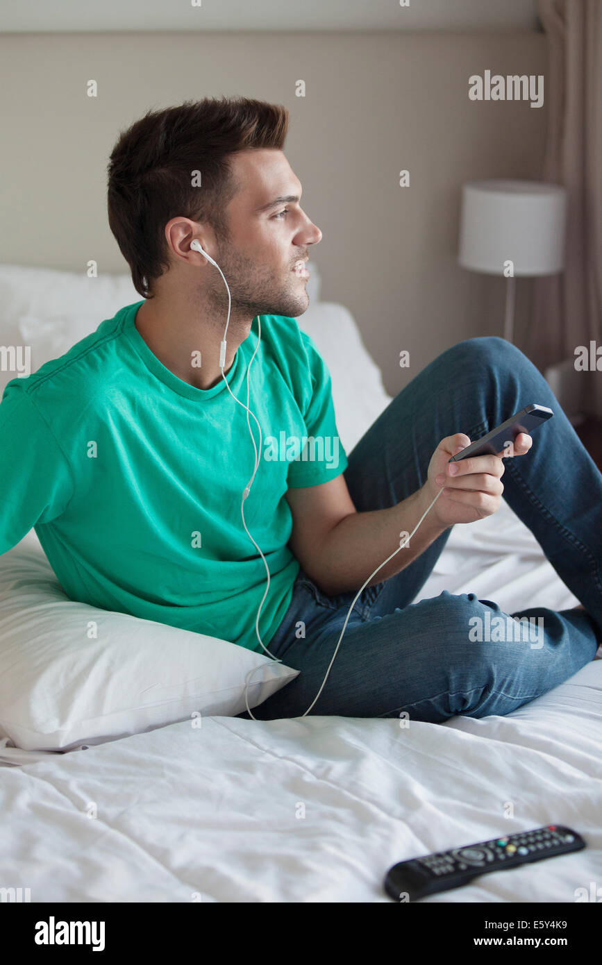 Young man sitting on bed listening to music with smartphone Stock Photo