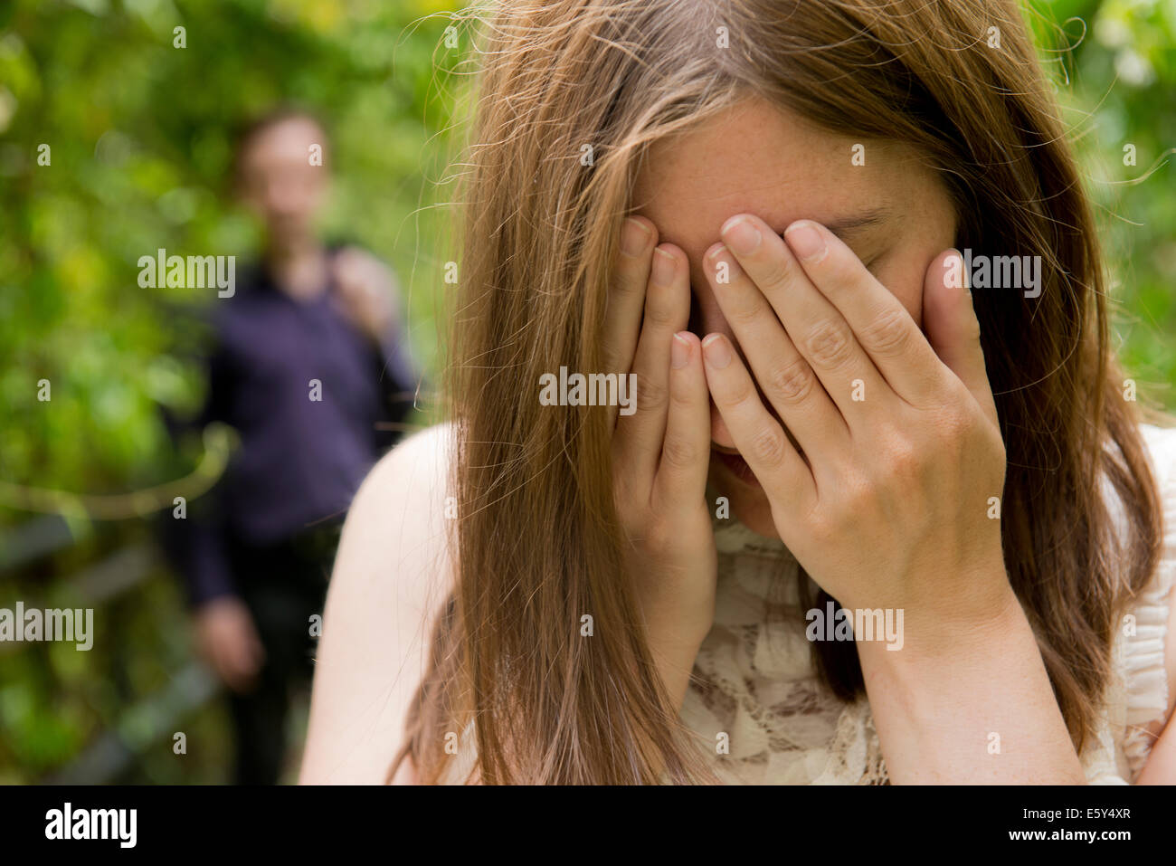 Tearful woman with hand on her face and man standing in the background. Stock Photo