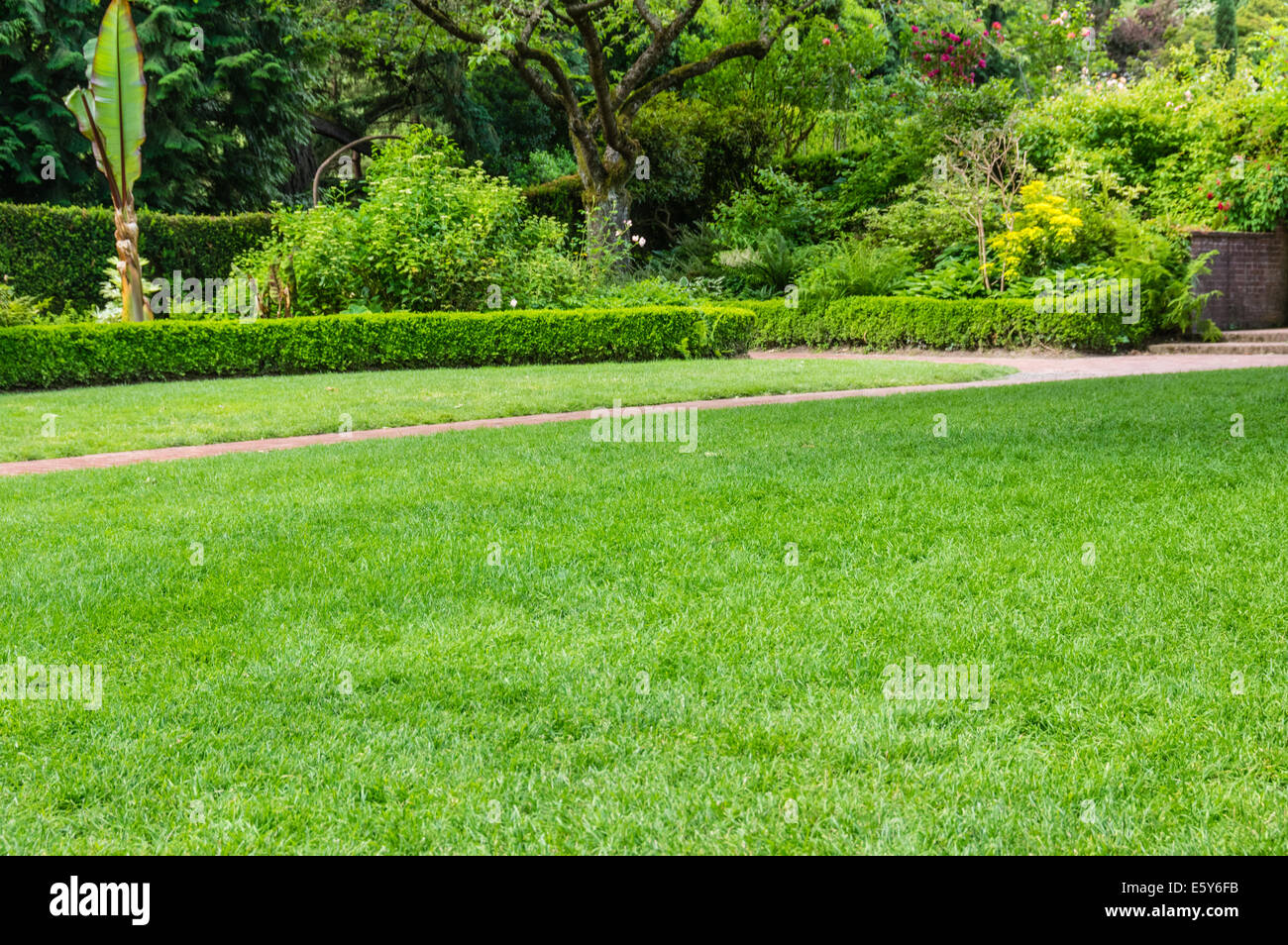 Green fresh lawn and brick pathway in a large public garden with hedges and flower beds Stock Photo