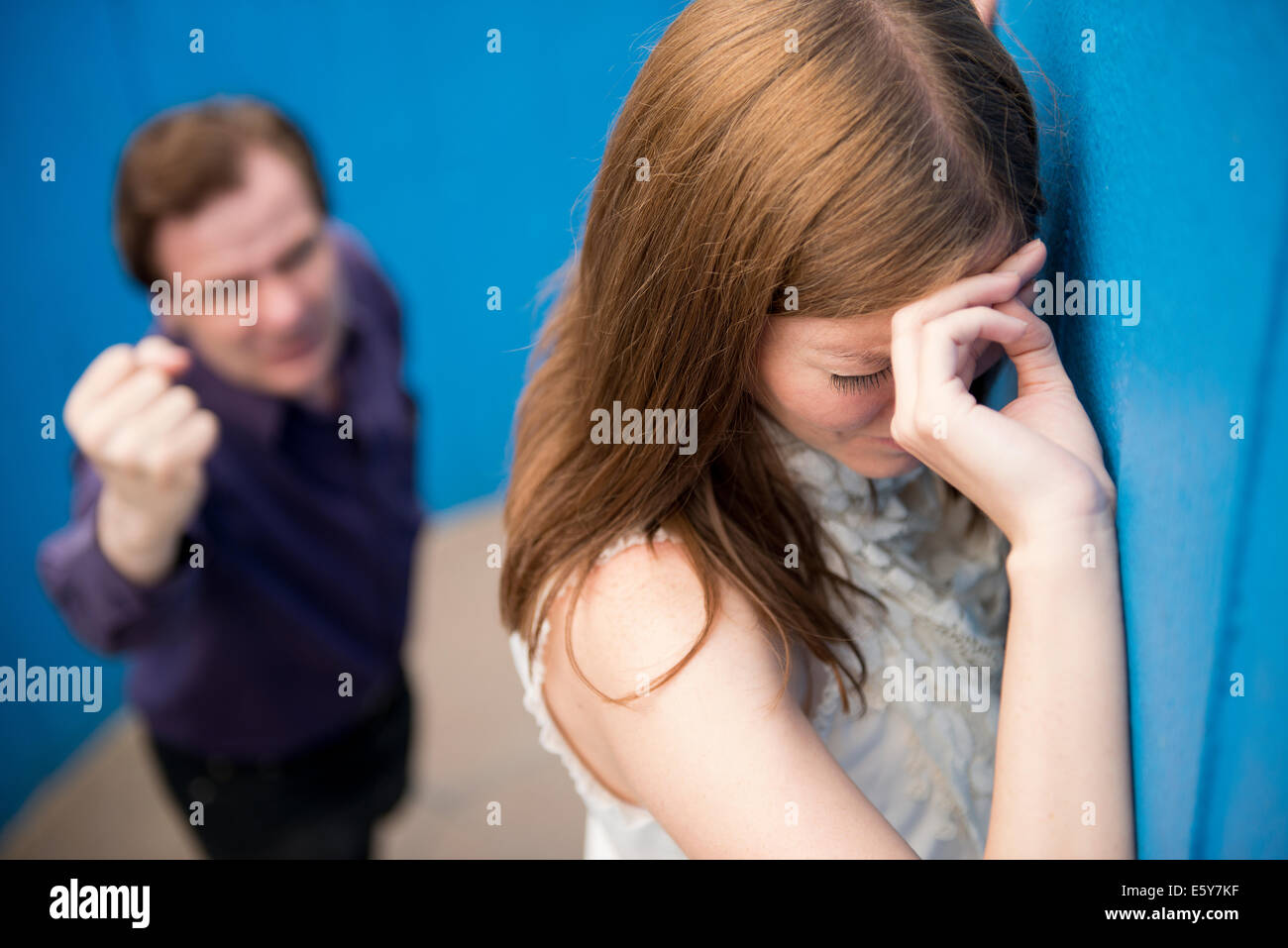 Tearful woman with her back to an aggressive man waving a clenched fist at her. Stock Photo